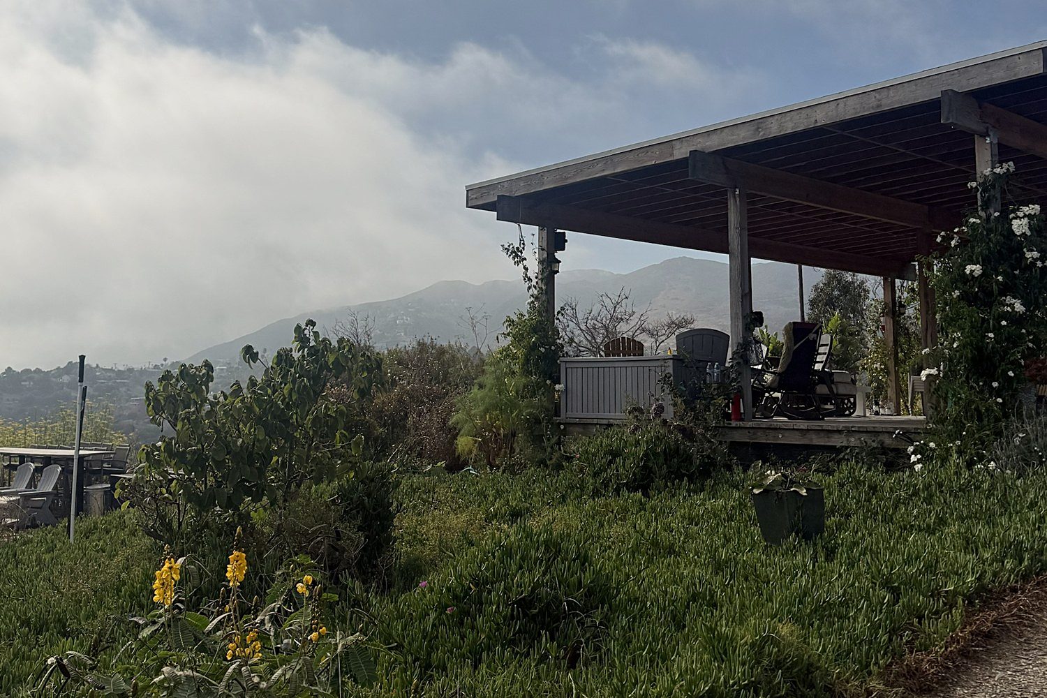 A covered porch and green hillside at Malibu Fig Farm, with mountains and low clouds behind
